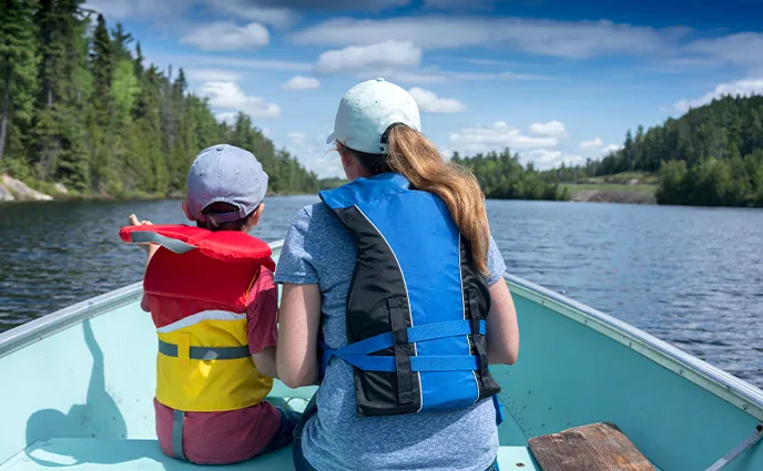Une femme et un enfant en gilet de sauvetage naviguent en chaloupe sur les eaux calmes d’un grand lac.