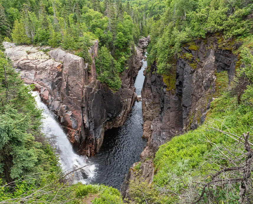Vue d'un canyon profond avec une cascade sur la gauche et une rivière calme au fond.