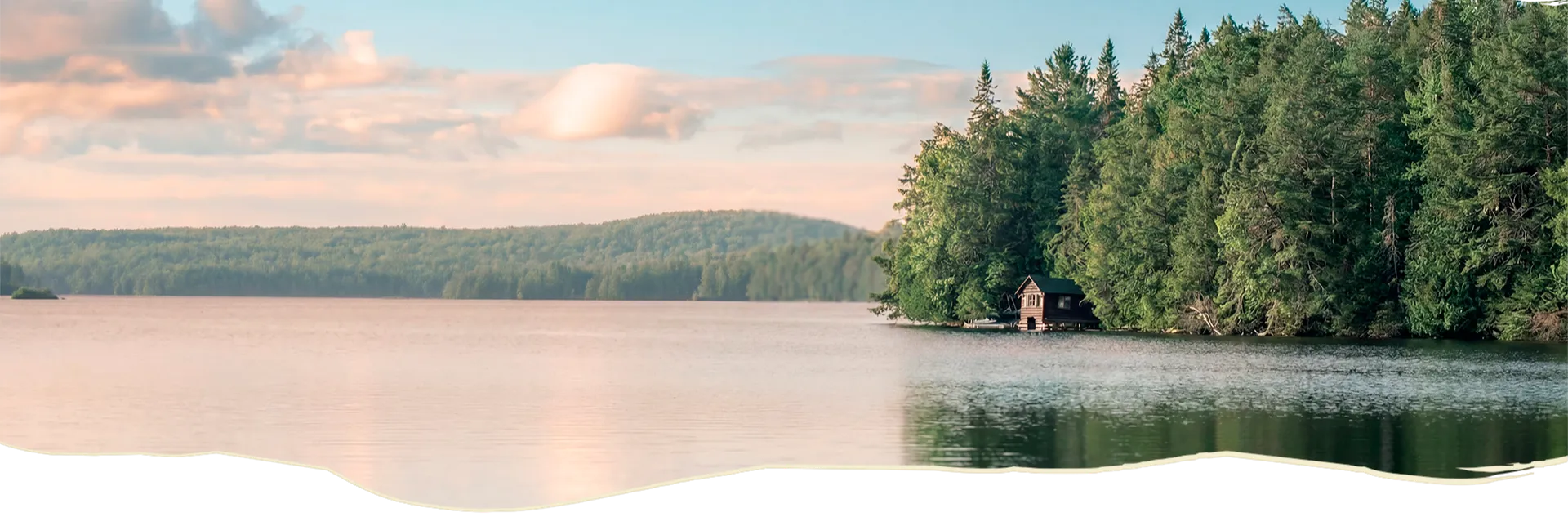 Une petite cabane en bois se cache au bord d’un lac calme et d'une grande forêt de sapins.