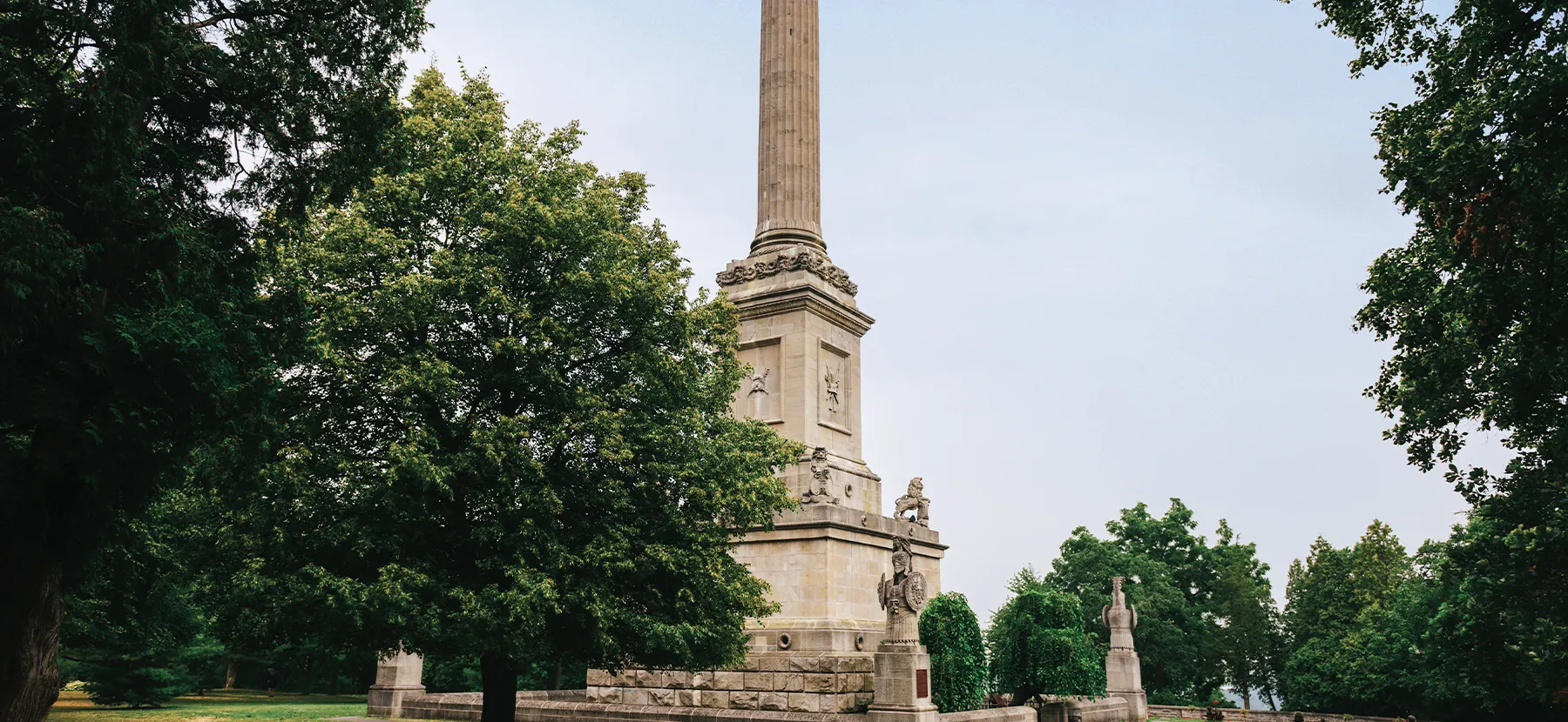 Un très grand monument en pierre en forme de haute colonne s’élève au milieu d’arbres et d'une pelouse verte.