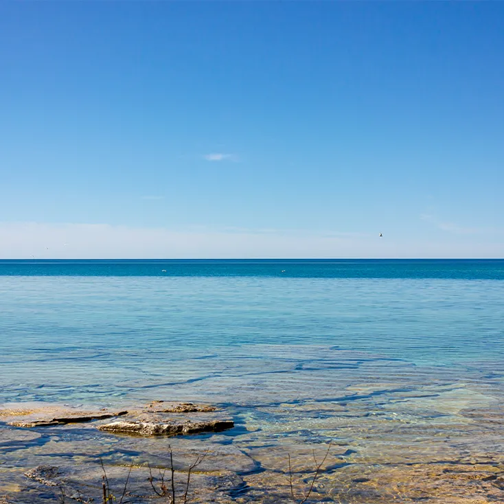 Grande étendue d’eau calme et transparente sous un ciel bleu, avec des rochers visibles au fond du lac.